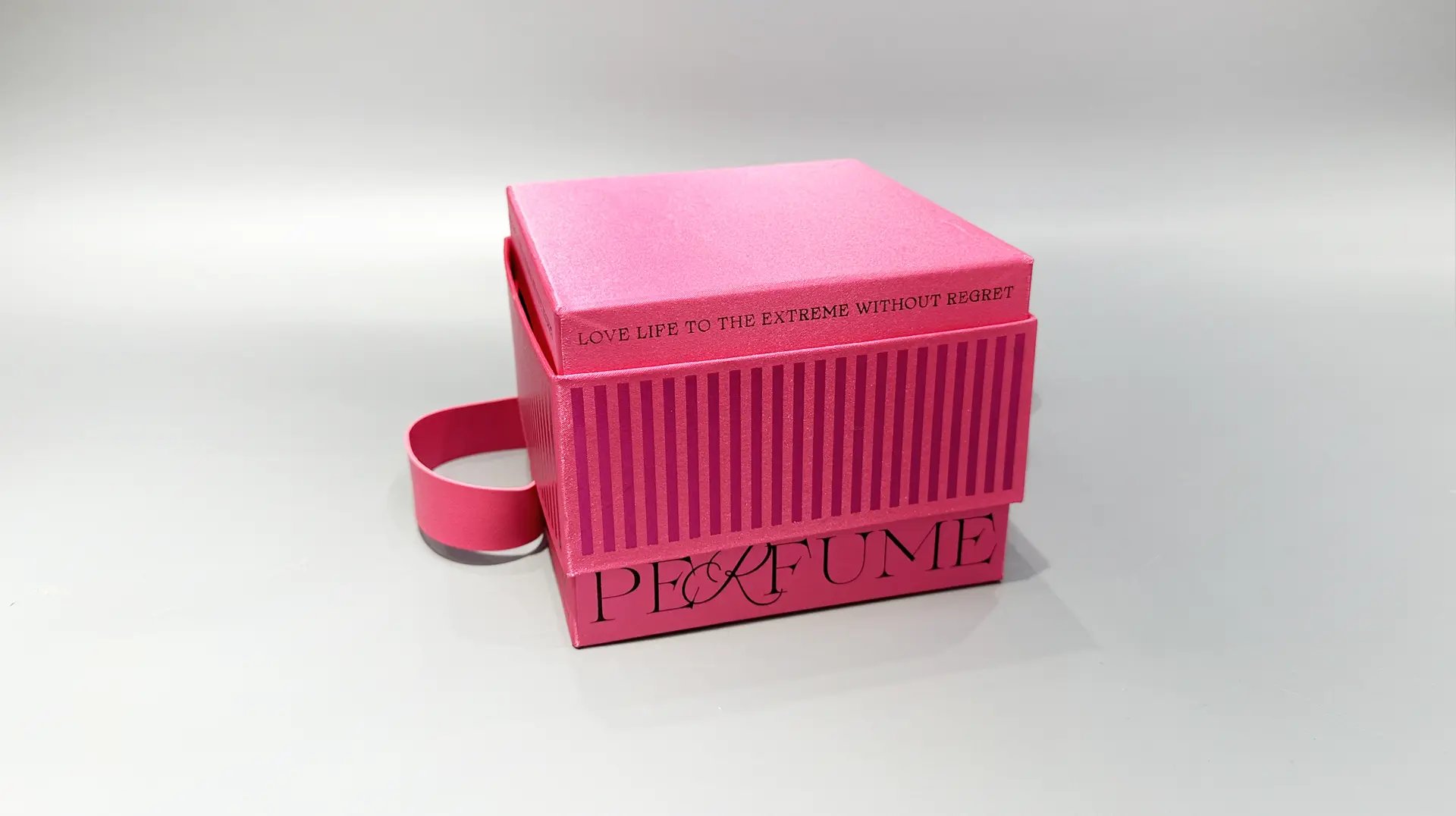 Certainly! Here’s a revised description of your product using packaging box terms:

This product is a vibrant, custom-designed perfume box characterized by its bright pink color and vertical stripe pattern. The box features a convenient strap handle for easy carrying and an elegantly designed lift-off lid. The front showcases carefully crafted typography that reflects the essence of the perfume inside.