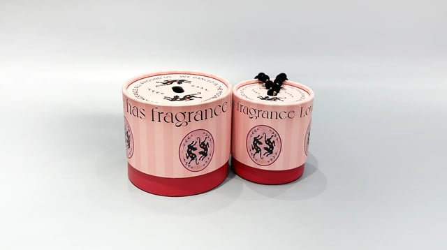 The image showcases our custom box packaging, featuring two elegantly designed pink cylindrical boxes with red bases. These containers are crafted to resemble sophisticated round-shaped packaging solutions. The arrangement includes one slightly smaller cylinder positioned next to the larger one, highlighting the versatility in size options we offer for personalized packaging needs.