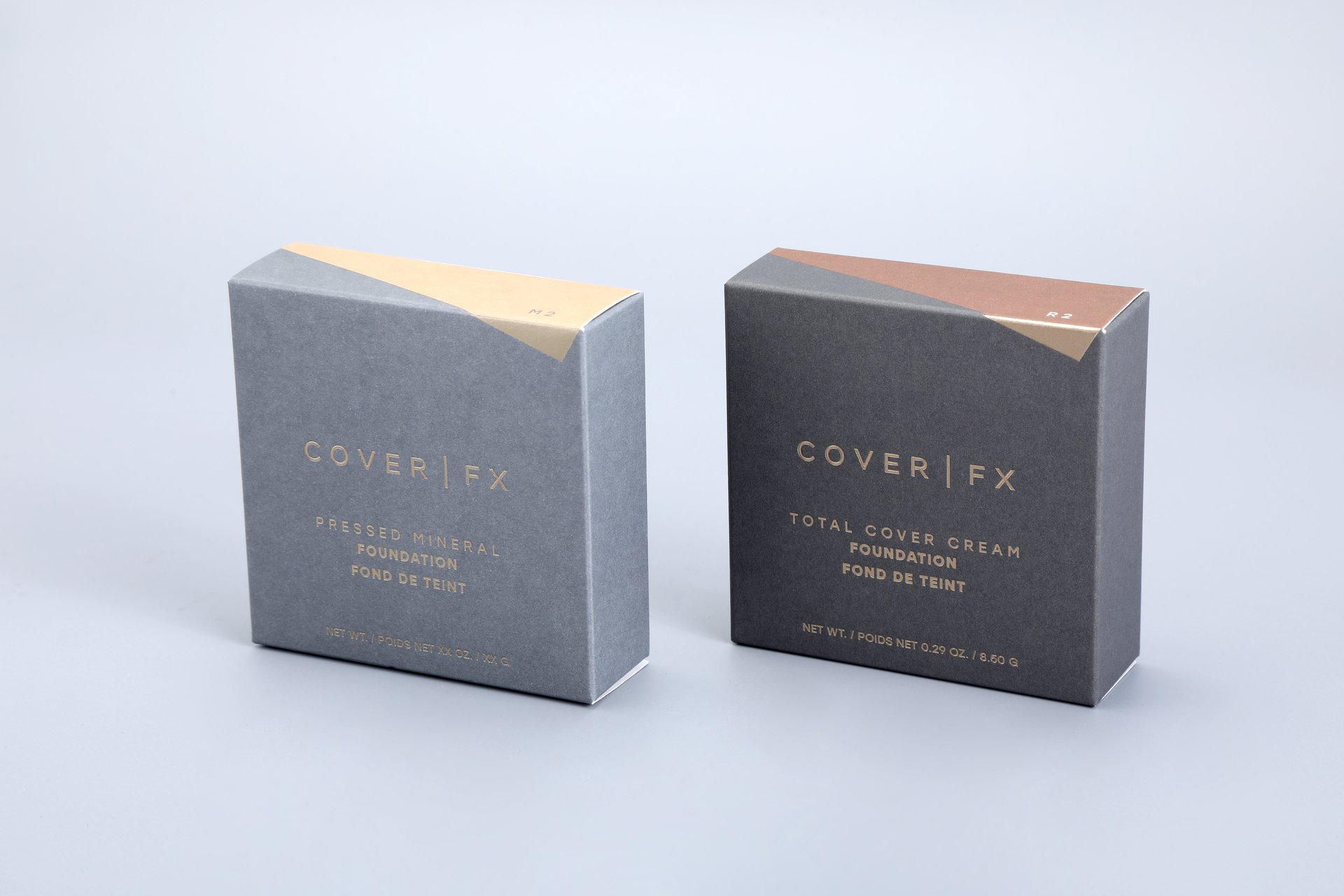 We produce custom packaging solutions. This image showcases our product, featuring two distinct boxes designed for foundation products. One box is tailored for a pressed mineral foundation, while the other is crafted to house a total cover cream foundation, all set against a sleek gray backdrop.