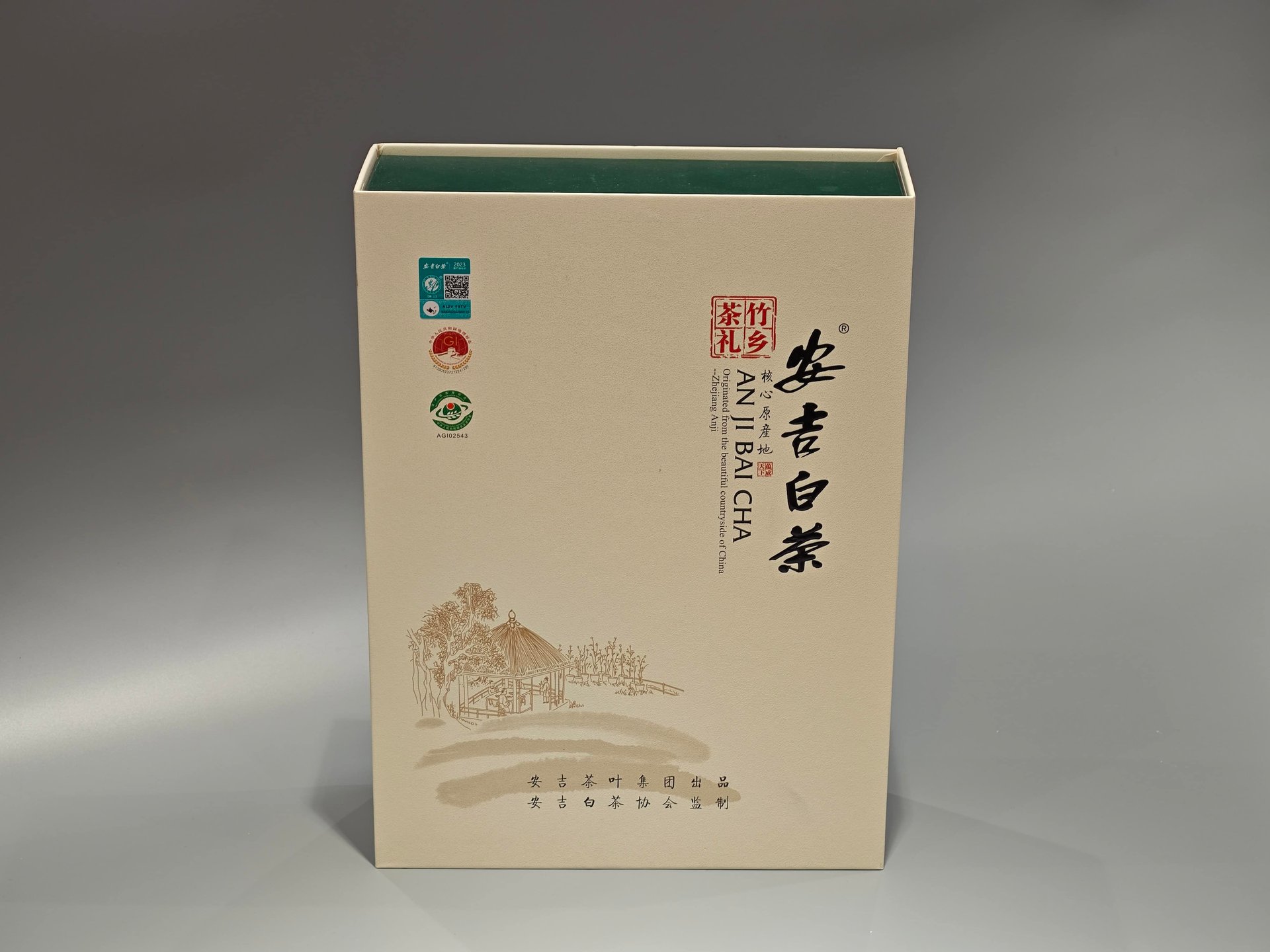 This image represents our custom box packaging product for Anji Bai Cha tea. The design features an elegant representation of Chinese calligraphy, distinctive logos, and an artistic illustration showcasing a serene landscape with a traditional hut surrounded by trees on the front.