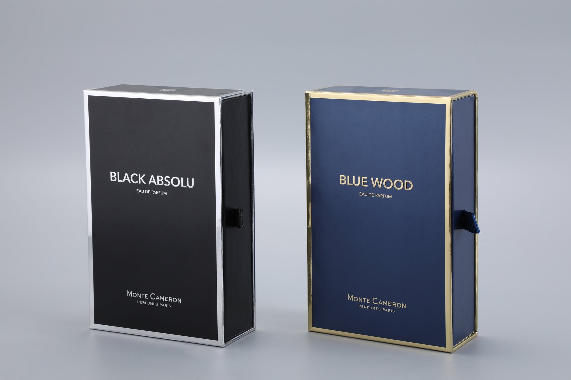 Two custom-designed boxes are displayed side by side, showcasing sophisticated packaging for perfume products. The box on the left features a sleek, dark aesthetic, while the box on the right presents a contrasting bold blue design. Both boxes exemplify premium craftsmanship and branding from a renowned Parisian perfume house.